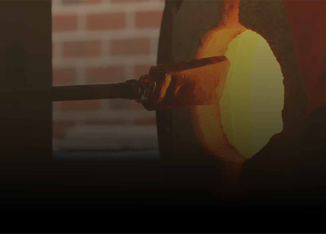 A glass blowing student pulls a piece of glass out of the kiln on a blowing rod.
